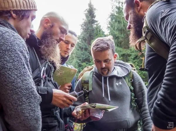 Gruppe von fünf Personen betrachtet Karten und ein Gerät im Wald