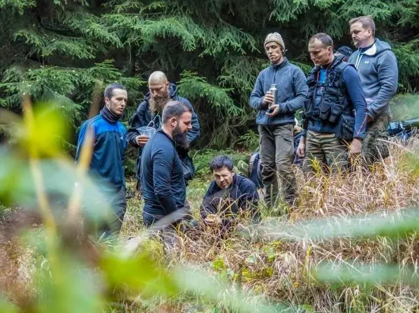 Gruppe von Personen steht um einen Bodenbereich in einem Wald