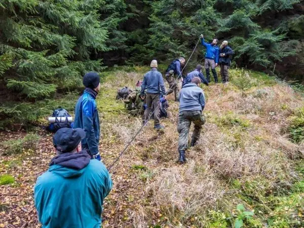 Gruppe zieht eine Last mit einem Seil durch das Gras im Wald beim Survival Training