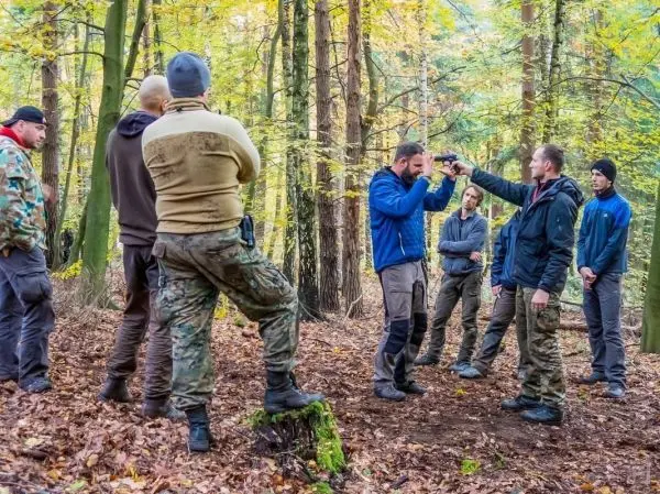 Gruppendynamik im Wald, eine Person demonstriert eine Technik mit einer Waffe
