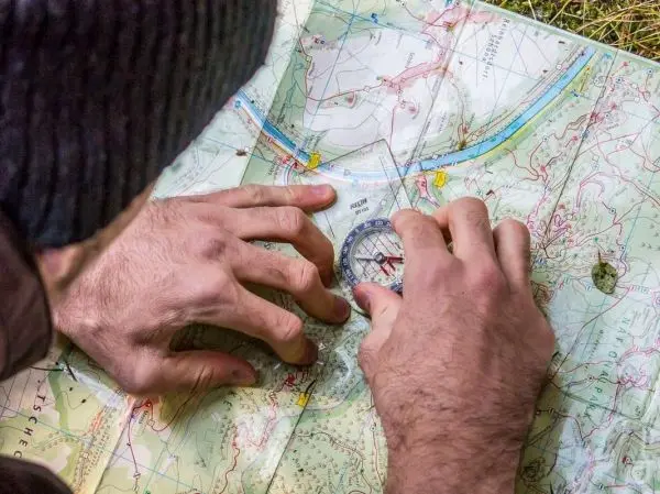 Hände legen einen Kompass auf eine topografische Karte zur Orientierung