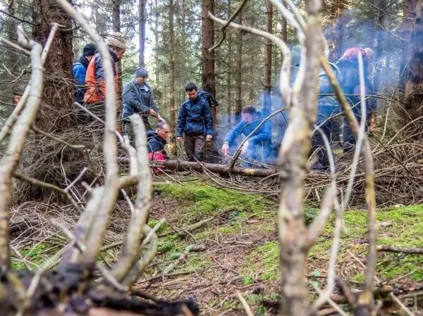 Kleine Flamme erzeugt Rauch im Wald, während mehrere Personen um das Feuer stehen
