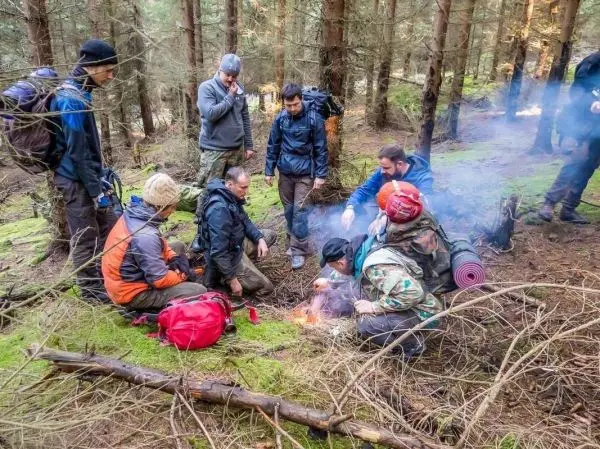 Kleine Flamme glimmt im Wald, Gruppe um Feuer versammelt