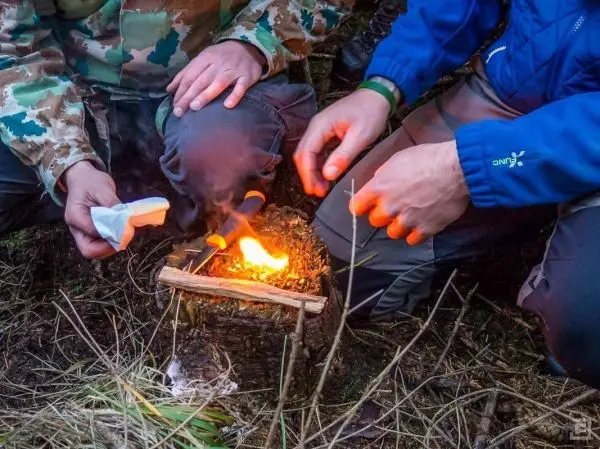 Kleine Flamme lodert aus einem Zundernest, Hände halten Zunder bereit