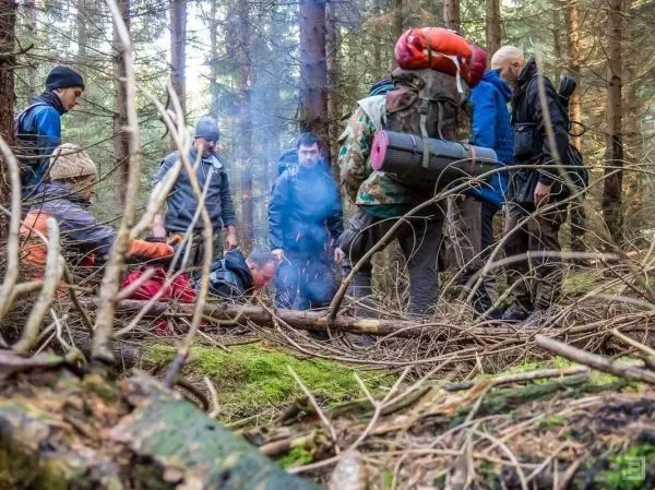 Kleine Flamme raucht zwischen mehreren Personen im Wald, die um ein Feuer versammelt sind