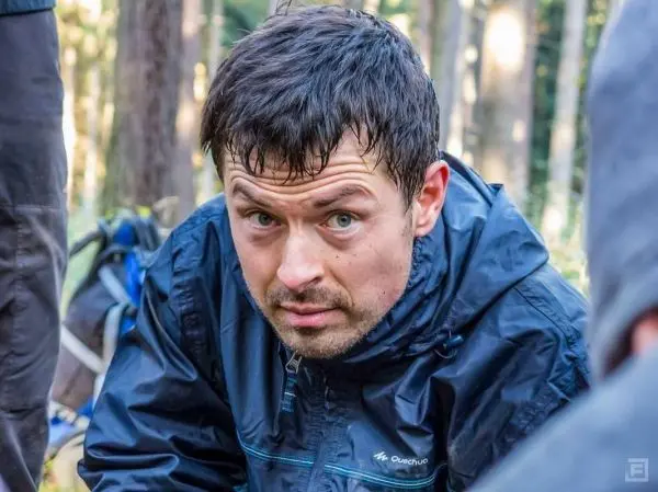 Kneeling in the forest, ein Mann betrachtet konzentriert eine Ausrüstung