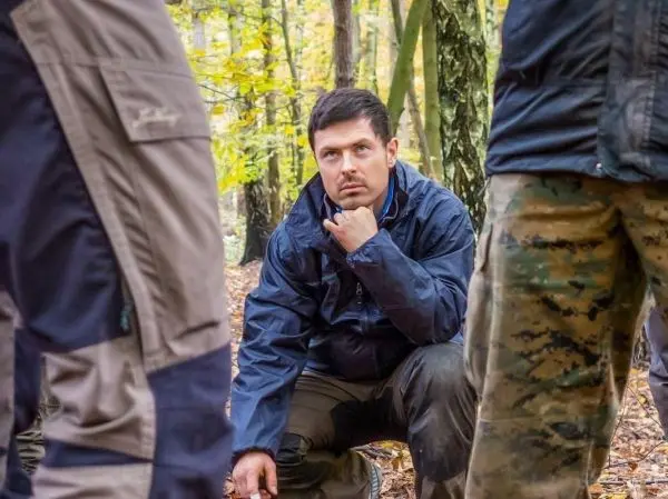 Kniend betrachtet ein Mann den Boden im Wald, umgeben von anderen Personen