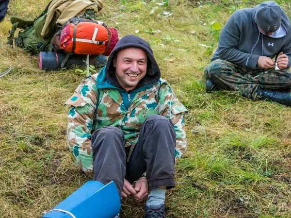 Lächelnder Mann sitzt auf dem Boden und trägt eine camouflierte Jacke