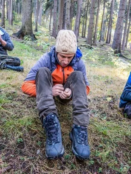 Mann sitzt im Wald und bearbeitet ein Stück Holz mit einem Messer
