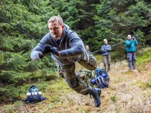 Mann überquert selbstgebaute Seilbrücke, während andere ihn sichern
