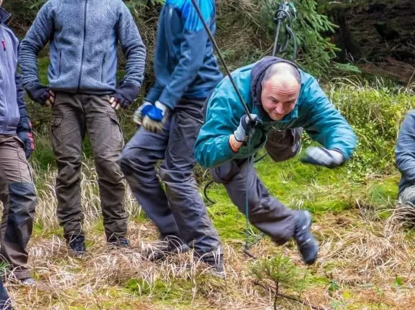 Mann überquert selbstgebaute Seilbrücke, während andere ihn unterstützen