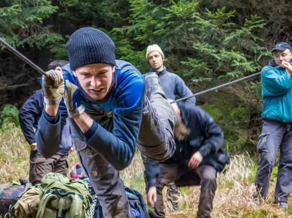 Mann überquert selbstgebaute Seilbrücke, während andere im Hintergrund beobachten