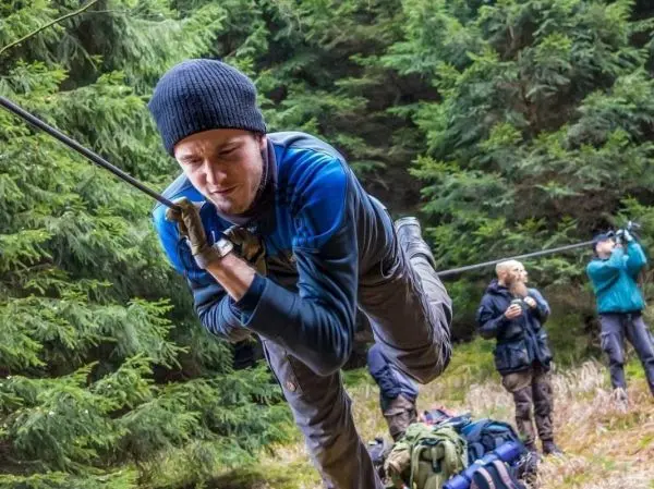 Mann überquert selbstgebaute Seilbrücke, während andere im Hintergrund beobachten