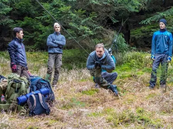 Mann überquert selbstgebaute Seilbrücke, während andere zuschauen