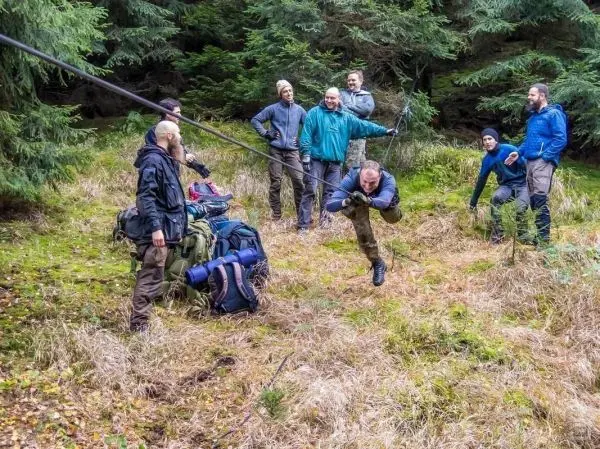 Mann überquert selbstgebaute Seilbrücke, während andere zuschauen