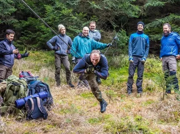Mann überquert selbstgebaute Seilbrücke, während Gruppe zuschaut