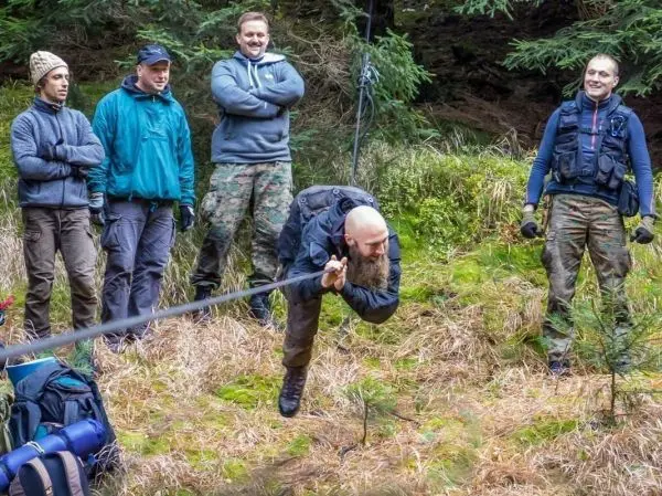 Mann zieht an einem Seil während andere zuschauen, im Wald auf Grasboden