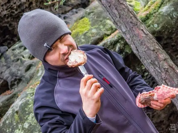 Person hält ein Stück Fleisch auf einem Spieß und beißt hinein