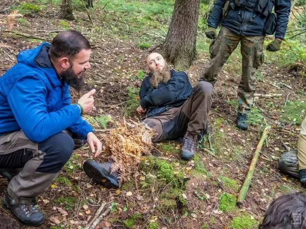 Person spricht mit sitzender Person im Wald beim Überlebenstraining