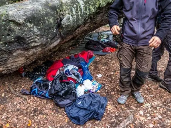 Person steht neben verstreuter Ausrüstung unter einem Felsen