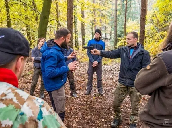 Person zeigt anderen Teilnehmern den Umgang mit einer Pistole im Wald