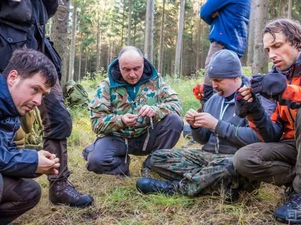 Personen sitzen im Wald und arbeiten mit kleinen Gegenständen beim Überlebenstraining