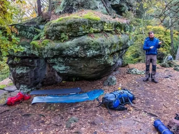 Rucksack und Isomatten liegen auf dem Boden, während eine Person Ausrüstung prüft