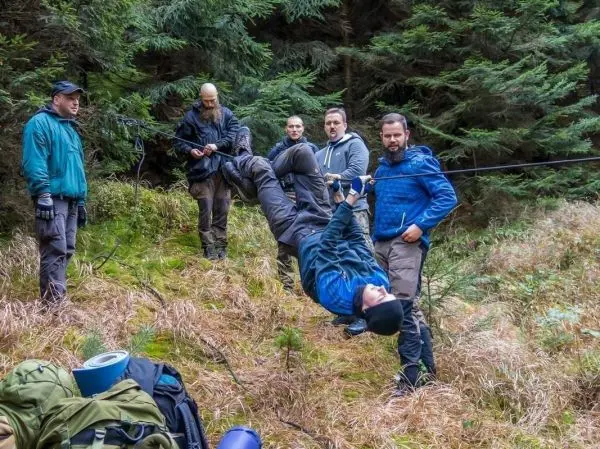 Teilnehmer überquert eine selbstgebaute Seilbrücke mit Unterstützung