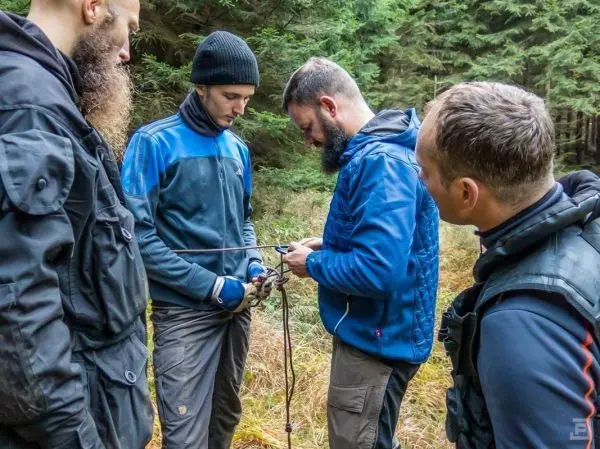 Vier Personen arbeiten gemeinsam an einer Seiltechnik im Wald