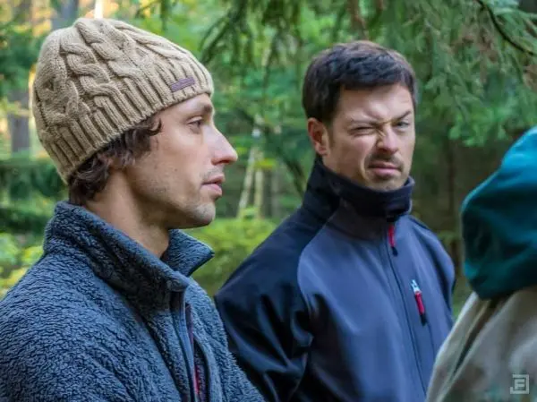 Zwei Männer in Outdoor-Bekleidung stehen im Wald, einer blinzelt