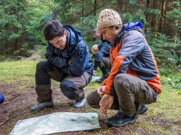 Zwei Personen betrachten eine Karte auf dem Boden im Wald