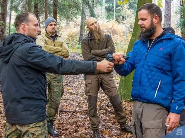 Zwei Personen demonstrieren den Umgang mit einer Waffe, während andere zuschauen