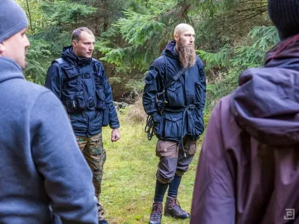 Zwei Personen in taktischer Kleidung stehen im Wald und beobachten die Umgebung