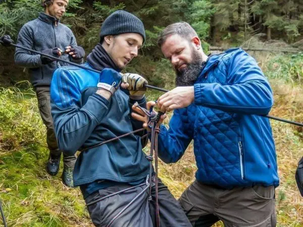 Zwei Personen knoten Seile für eine Seilquerung im Wald
