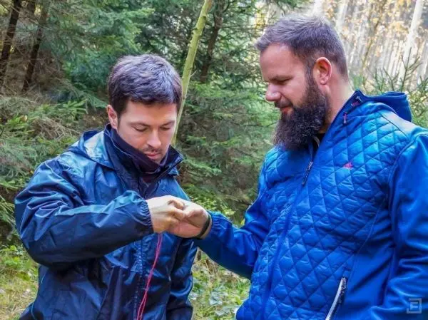 Zwei Personen stehen im Wald und zeigen auf einen Gegenstand in der Hand des einen