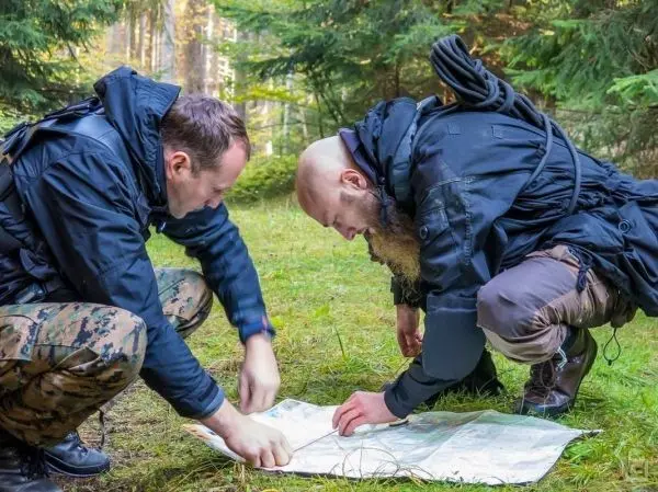 Zwei Personen studieren eine Karte auf dem Boden im Wald