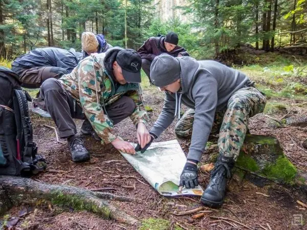 Zwei Personen studieren eine Karte auf dem Waldboden, Rucksäcke im Hintergrund