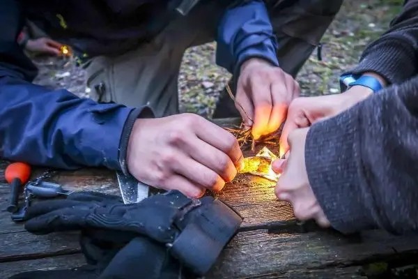 Hände entzünden Feuer mit Zunder und Funken beim Survival Training