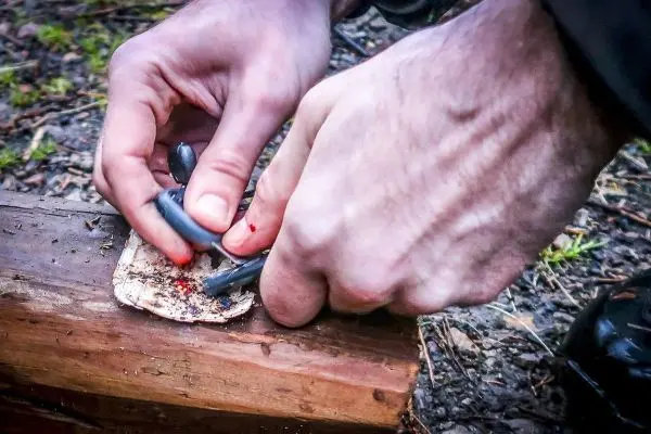Hände nutzen einen Schaber, um Zunder auf einem Holzstück zu bearbeiten