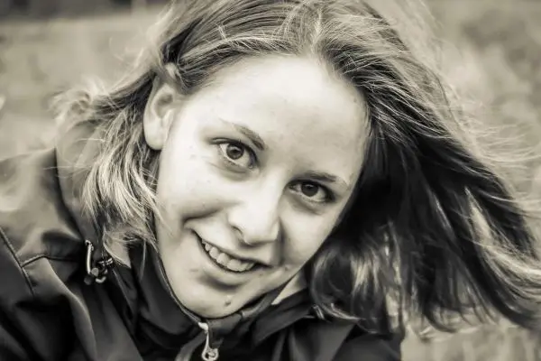 Lächelnde Person mit windgepeitschtem Haar in dunkler Jacke