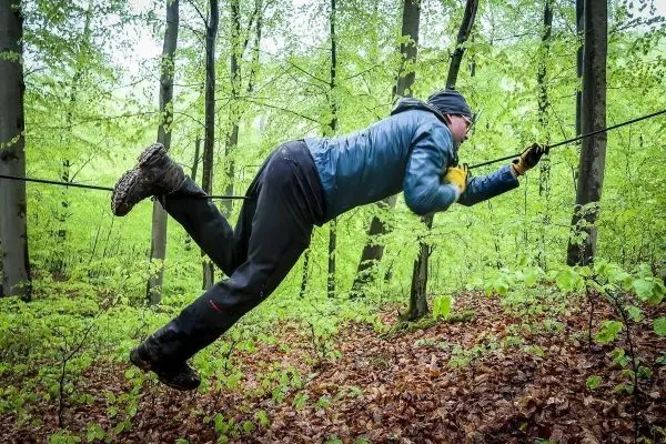 Mann überquert selbstgebaute Seilbrücke zwischen Bäumen im Wald