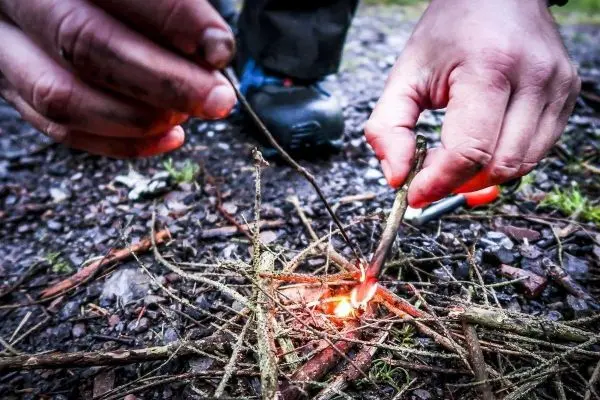 Person entzündet kleine Äste mit einem Stock beim Survival Training