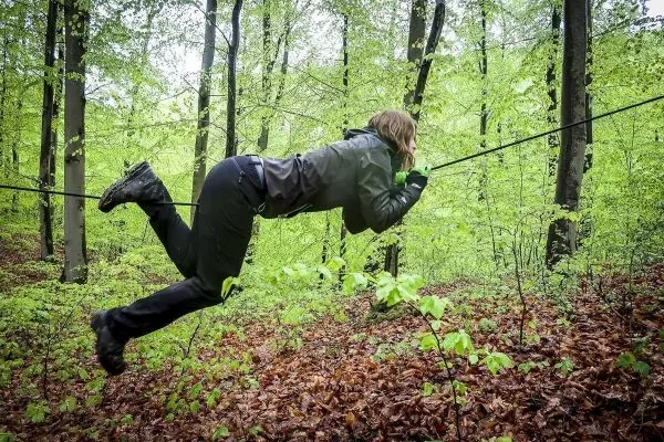 Person schwingt an selbstgebauter Seilbrücke durch den Wald beim Survival Training