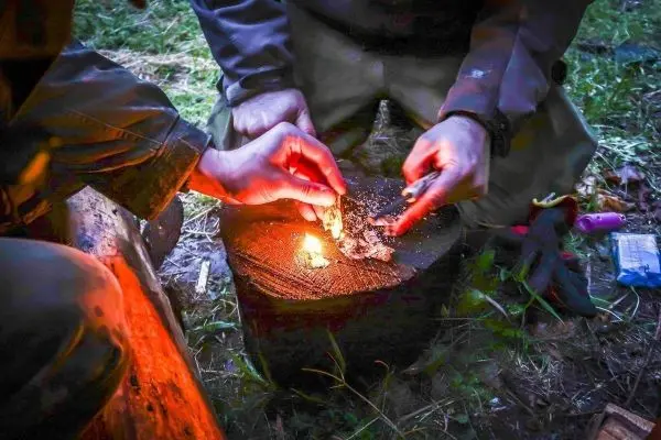 Zunder glimmt auf einem Holzstück, während Hände Funken erzeugen