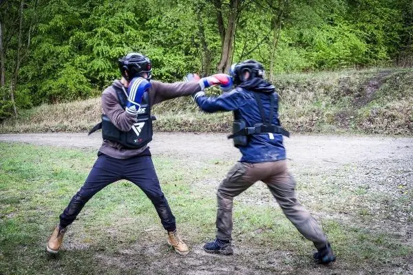 Zwei Personen in Schutzausrüstung führen einen Boxkampf auf einem unebenen Boden