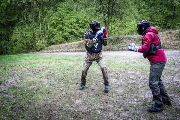 Zwei Personen in Schutzausrüstung üben Boxtechniken auf einem unebenen Boden