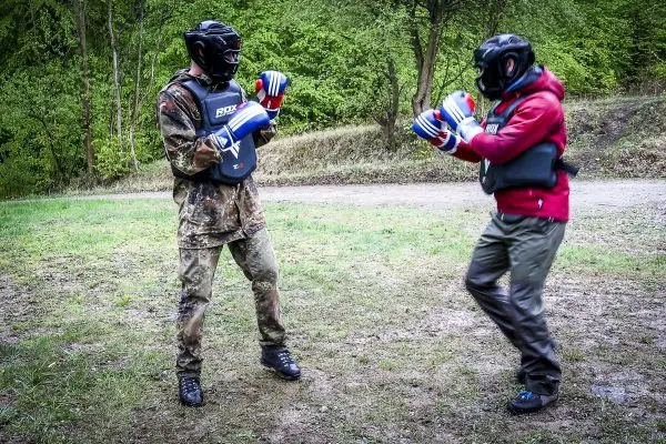 Zwei Personen in Schutzausrüstung üben Kampfsporttechniken auf einer Wiese