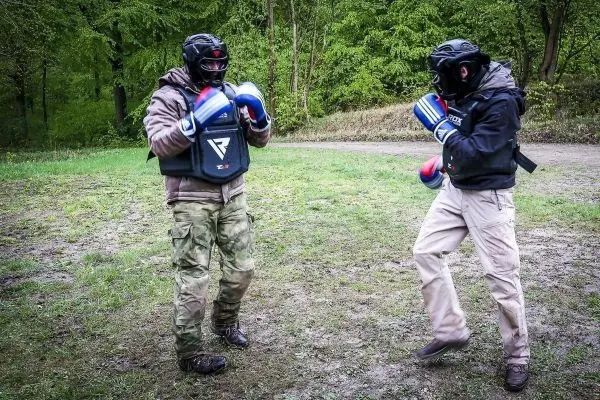 Zwei Personen in Schutzausrüstung üben Kampfsporttechniken auf einer Wiese