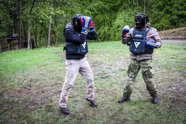 Zwei Personen in Schutzausrüstung üben Kampftechniken auf einer Wiese