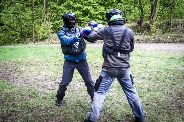 Zwei Personen in Schutzausrüstung üben Kampftechniken auf einer Wiese